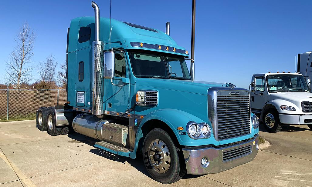 Blue Cascadia truck parked near trees.